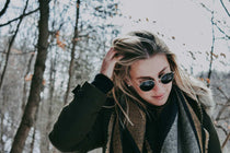 Jeune femme blonde qui se passe la main dans les cheveux et habillée avec une tenue d'hiver et des lunettes de soleil