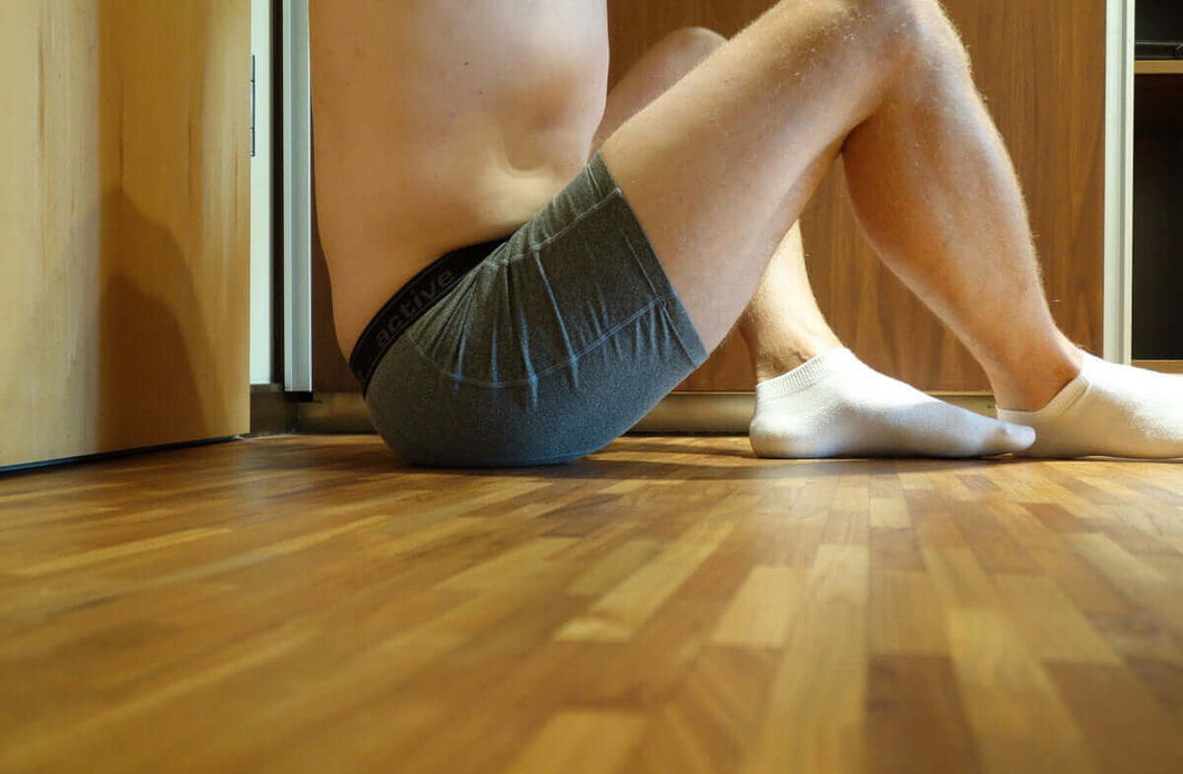 Homme en boxer gris et mini chaussettes assis sur un parquet en bois clair